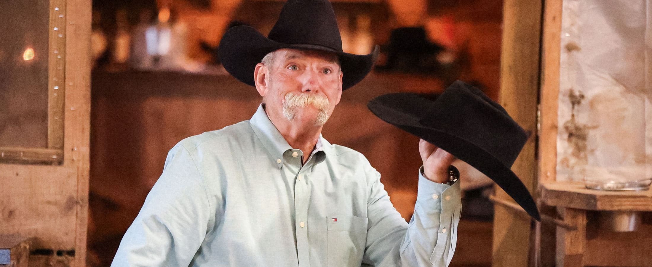 A cowboy with a gray mustache, wearing a black cowboy hat and holding a black cowboy hat.
